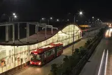 Autobús articulado rojo en una estación moderna del sistema BRT iluminada de noche.