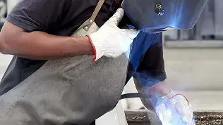 Operario realizando trabajos de soldadura en un entorno industrial para la fabricación de componentes de puertas automáticas.