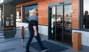 Puerta automática corredera de cristal en la entrada de un establecimiento comercial con fachada de madera.