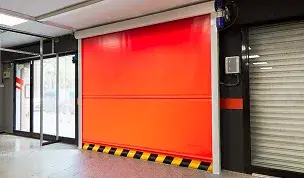 Puerta rápida enrollable de lona roja en un entorno industrial con banda de seguridad inferior rayada en amarillo y negro.