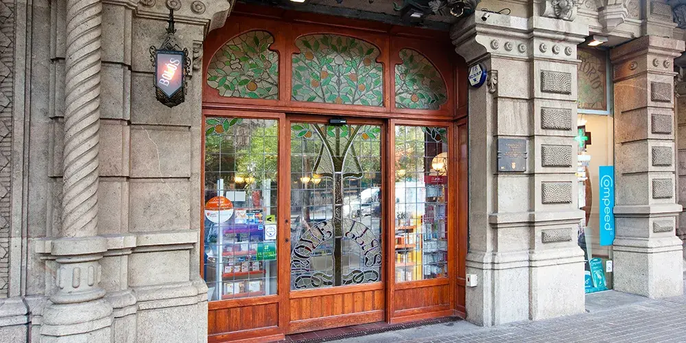 porta in legno in stile modernista con vetrate decorative a motivi vegetali e colonne in pietra scolpita.