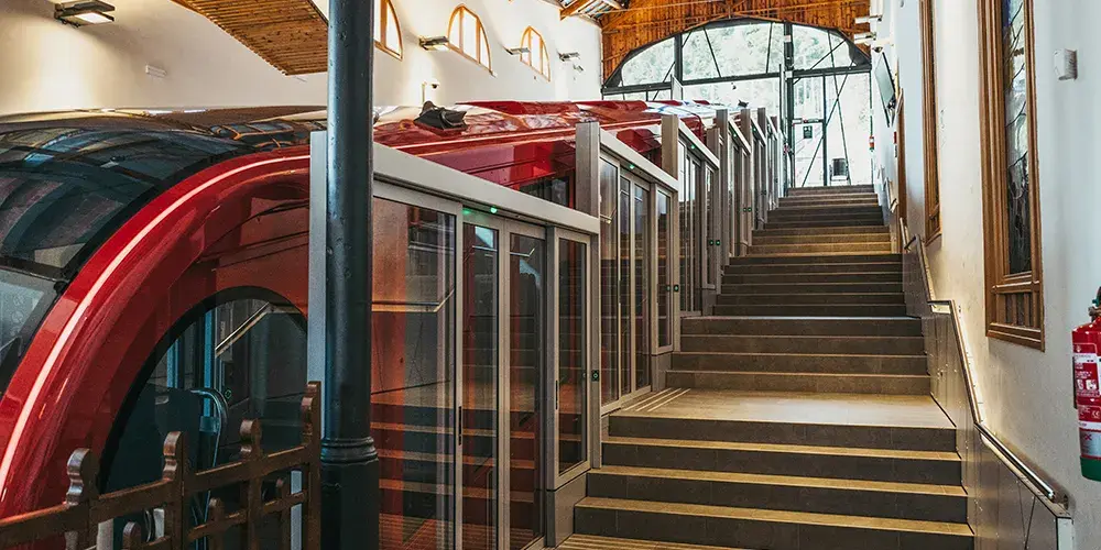 Interno di una stazione con una funicolare rossa moderna e porte automatiche in vetro lungo la banchina con scala laterale.